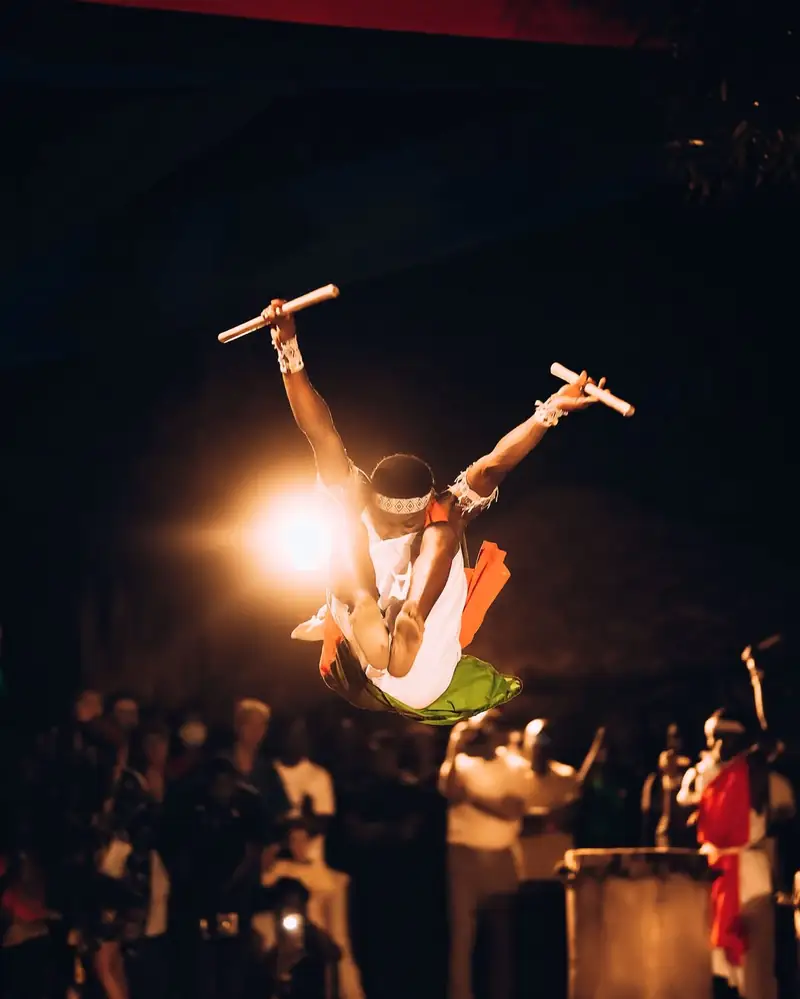 Un danseur en plein saut, bâtons levés, au-dessus du public