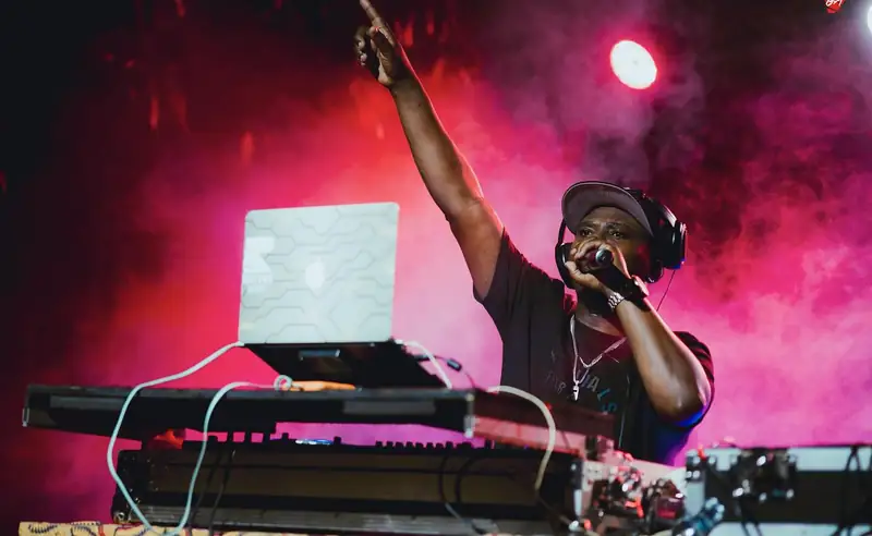 Un DJ lève le bras derrière ses platines, lumière rose